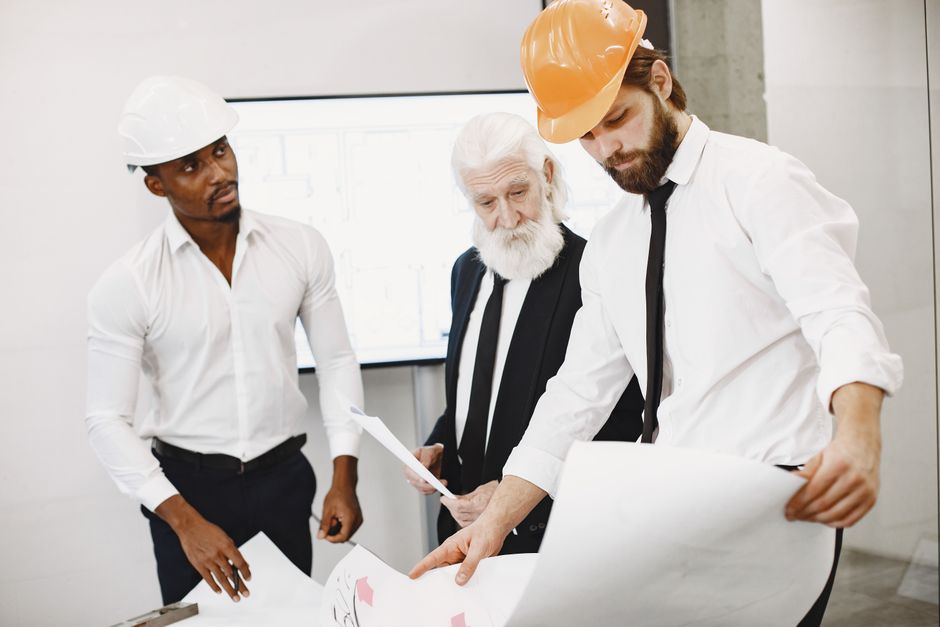 A diverse team of architects collaborates on a project, examining blueprints together in a modern office setting.