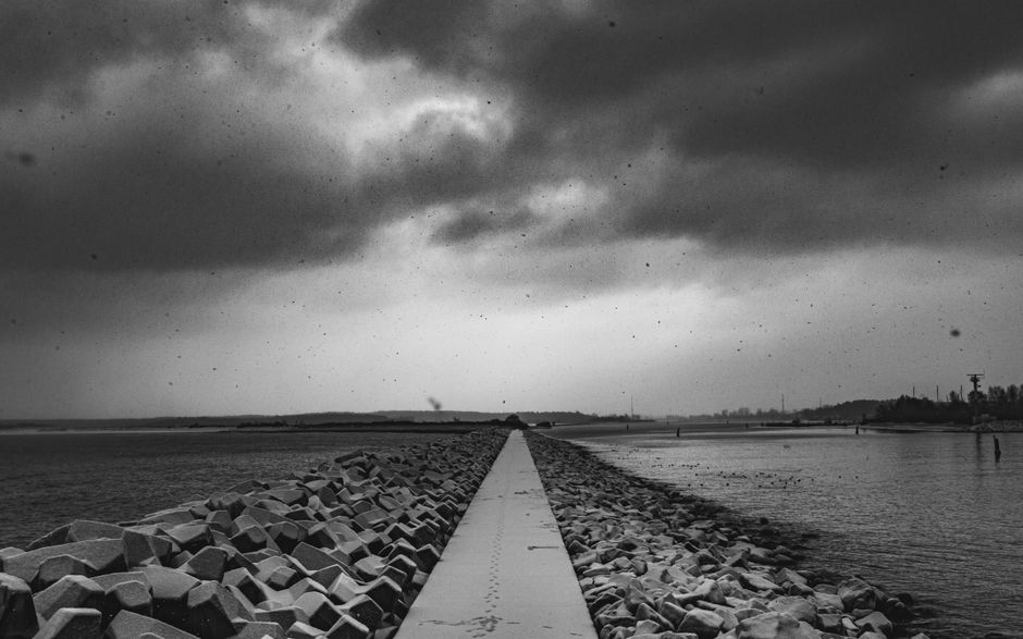 Moody black and white seascape showcasing a breakwater under a cloudy sky.